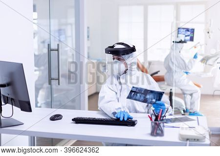 Dentist Nurse Dressed In Ppe Suit Holding Patient Teeth X-ray During Covid-19. Medicine Team Wearing