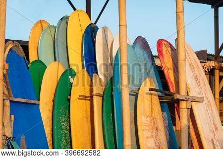Set Of Different Color Surf Boards In A Stack By Ocean.bali.indonesia. Surf Boards On Sandy Beach Fo
