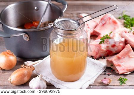 Passing The Bone Broth Through A Sieve. Concentrated Bone Broth In A Glass Jar