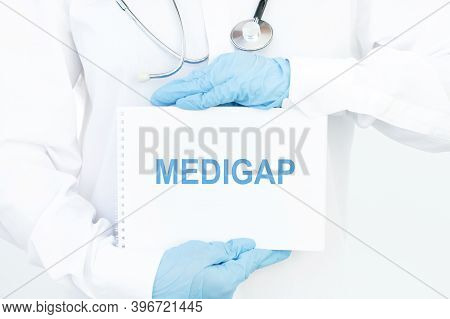 Doctor Holds A Card With The Name Of The Diagnosis Medigap. Medical Concept.