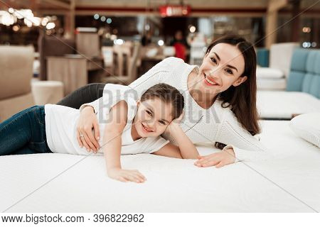 Young Beautiful Woman With Cute Little Girl Lies On Bed In Mattress Store.