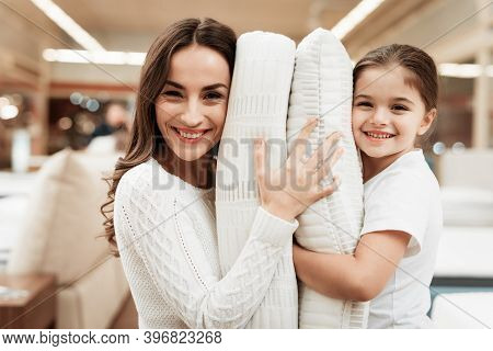 Smiling Little Girl With Beautiful Mother Hugs Pillows In Store Of Orthopedic Mattresses.