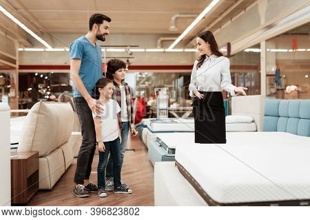 Young Girl Consultant Demonstrates Orthopedic Mattress To Young Father With Children In Furniture St