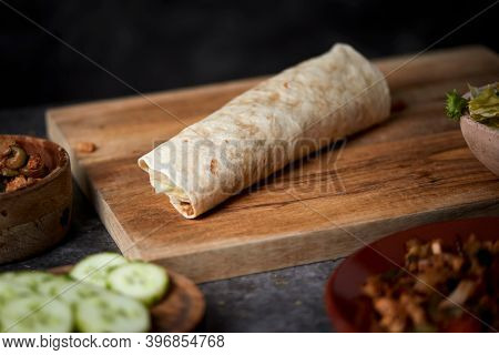 closeup of a durum or a burrito, filled with chicken meat cooked with different vegetables such as onion or red and green pepper, and fresh lettuce and cucumber, on a table