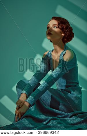 Art fashion. Portrait of a beautiful sensual lady in a long elegant dress sitting alone in the shade. Hair and makeup in the style of the 20s. 