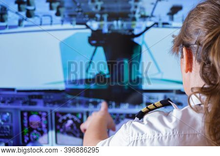 Beautiful woman pilot wearing uniform with epauletes changes the autopilot settings in the cockpit of a flying airplane