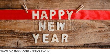 Happy New Year Inscription In Wooden Letters On A Wooden Background. The Word Happy On The Red Ribbo