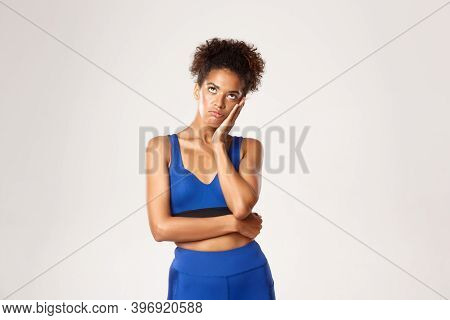 Studio Shot Of Bored Or Annoyed African-american Fitness Girl Roll Eyes Up And Leaning Head On Hand,