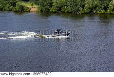 Speedboat Towing An Athlete On A Board Against The Background Of The Forest. Athlete Water Skiing An