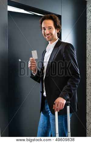Young business man standing with a keycard in front of a room door in a hotel