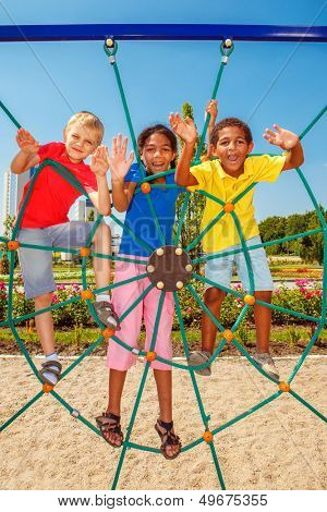 Cheerful friends climbing the net at a city playground
