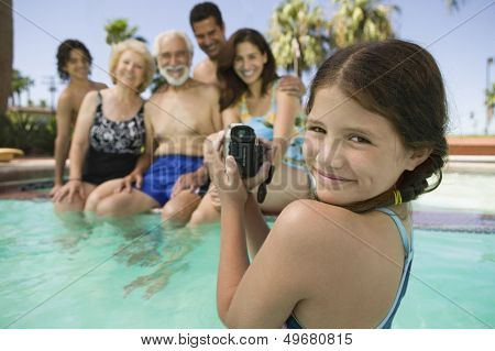 Portrait of smiling girl with video camera recording family in swimming pool