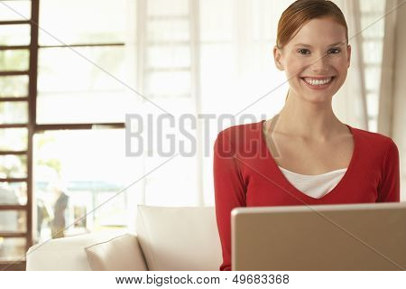 Portrait of happy young businesswoman with laptop sitting on chair in office lobby