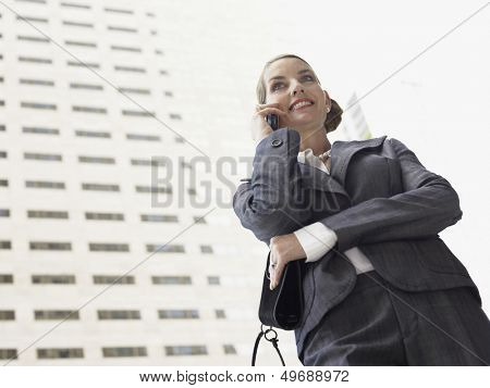 Low angle view of businesswoman using mobile phone against tall office building