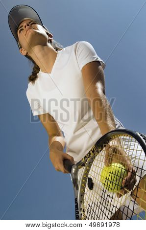 Low angle view of female tennis player holding ball and racket preparing to serve