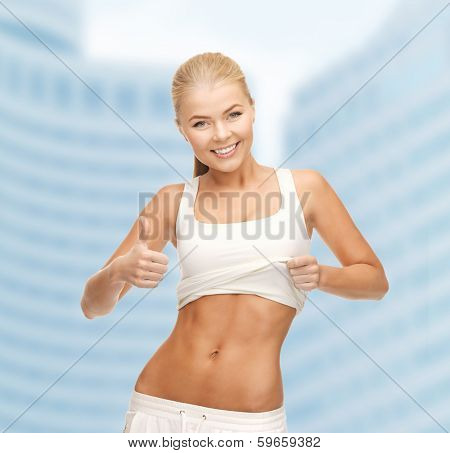 fitness and diet concept - beautiful sporty woman showing thumbs up and her abs