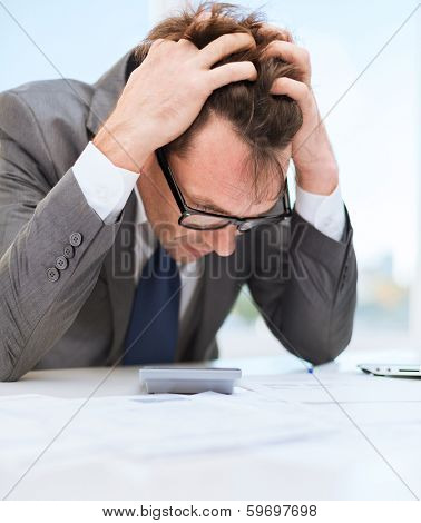 tax, business and stress concept - stressed businessman with papres, laptop and calculator