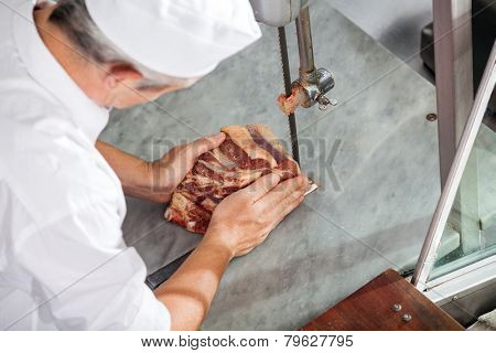 High angle view of butcher cutting fresh meat with bandsaw in butchery