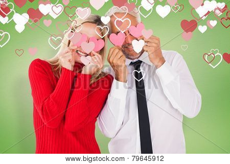 Silly couple holding hearts over their eyes against green vignette