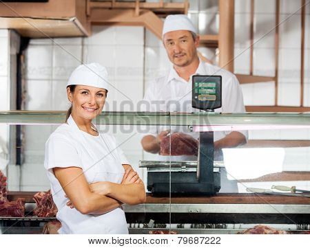 Portrait of confident female butcher with male colleague weighing meat at shop