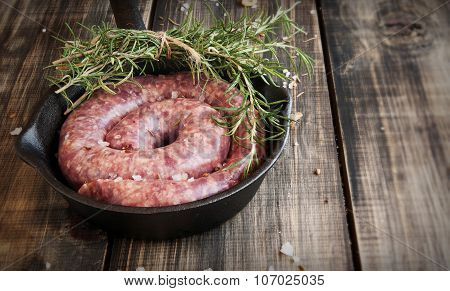raw beef sausages on a cast-iron pan with rosemary and spices,  wooden table, selective focus