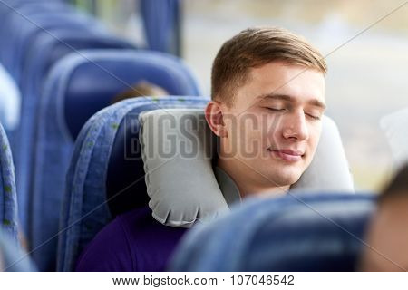 transport, tourism, road trip and people concept - happy young man sleeping in travel bus with pillow