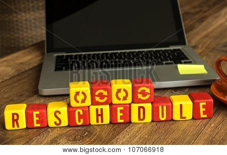 Reschedule written on a wooden cube in front of a laptop