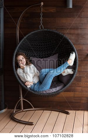  Young pretty smiling woman lying in rattan bubble chair using smart phone