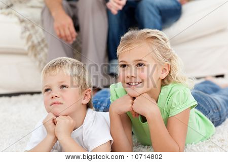 Hermano y hermana, viendo la televisión en el piso con sus padres