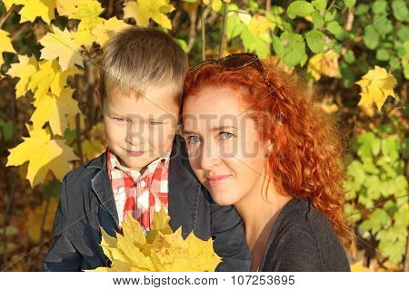 Mother And Little Son With Yellow Maples In Autumn Park At Sunny Day