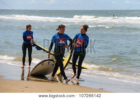 Young Surfer Friends In Wetsuits Walking Along The Shore With Their Surfing Boards. Zandvoort, The N