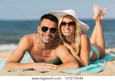 love, travel, tourism, summer and people concept - smiling couple on vacation in swimwear and sunglasses sunbathing on beach