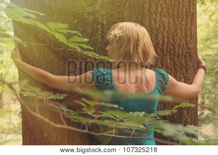 Young woman hugging the tree in forest. Post processed with vintage faded filter and sun flare.