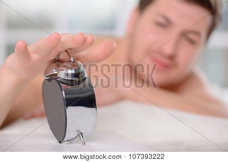 Young sleepy man turns off the alarm clock.