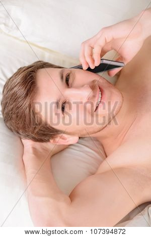 Guy lying in bed and speaking on mobile phone.