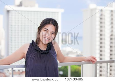 Biracial Teen Girl On Outdoor Highrise Patio, Urban Ocean  Background