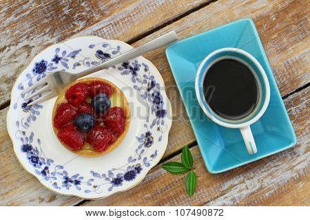 Crunchy tartelette with fresh fruit and cup of coffee on rustic wooden surface
