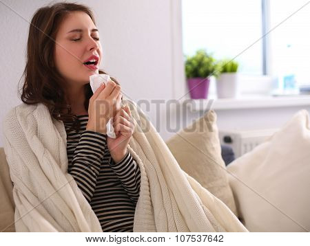 Portrait of a sick woman blowing her nose while sitting on the sofa