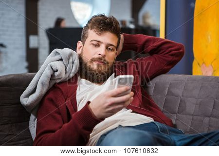 Relaxed young handsome attractive man lying grey on sofa and using cellphone