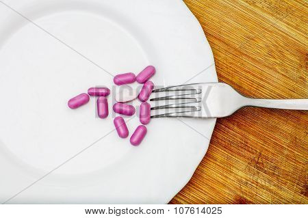 Diet concept with pink pills on white plate