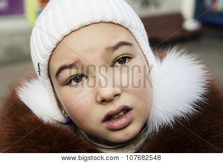Portrait of brown-eyed girl (9-10 years) in a knitted hat and fur jacket