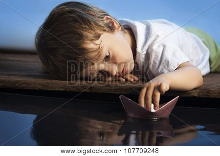 boy play in paper ship in water puddel