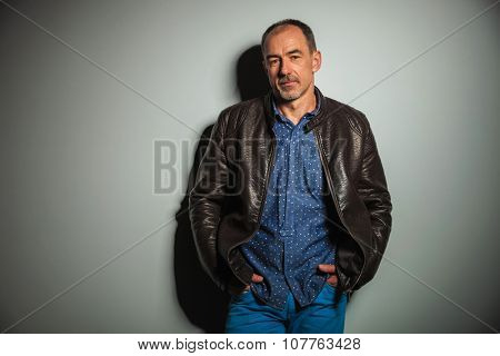 old casual man in leather jacket an jeans standing with hands in pockets instudio