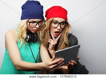 two hipster girls friends use digital tablet, studio shot over gray vackground