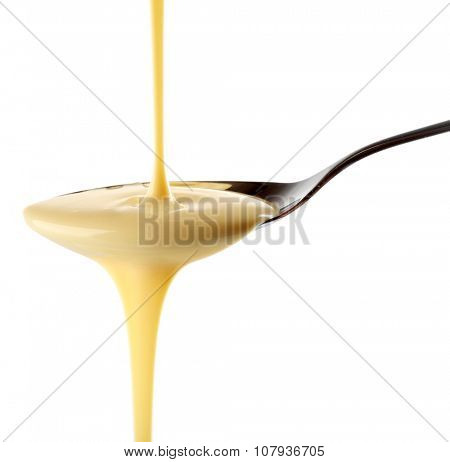 Condensed milk pouring from a spoon, isolated on white