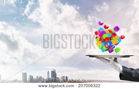 Cropped image of waiter's hand in white glove presenting multiple cubes on metal tray with cityscape view on background. 3D rendering.