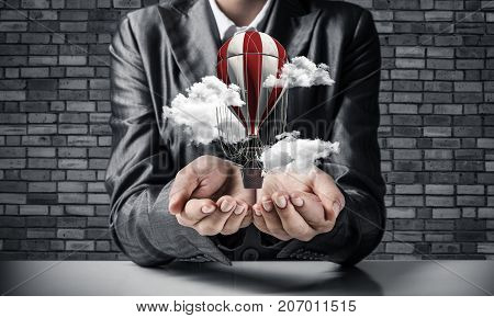 Closeup of business woman in suit presenting flying aerostate among clouds in her palms with dark brick wall on background. 3D rendering.