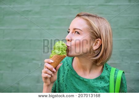 Young happy hipster woman in green lace dress eating ice cream on color background
