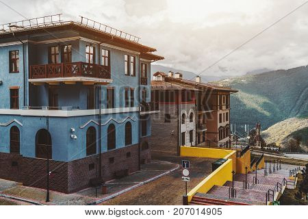 View of empty and neat streets of a small resort town on rain through sunshine with colorful hotels inns and walls; overgrown mountains in background with low clouds district of Sochi Russia