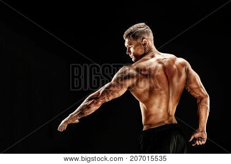 Very brawny guy bodybuilder posing. Beautiful sporty guy male power. Fitness muscled man showing his back in studio. Dark background.